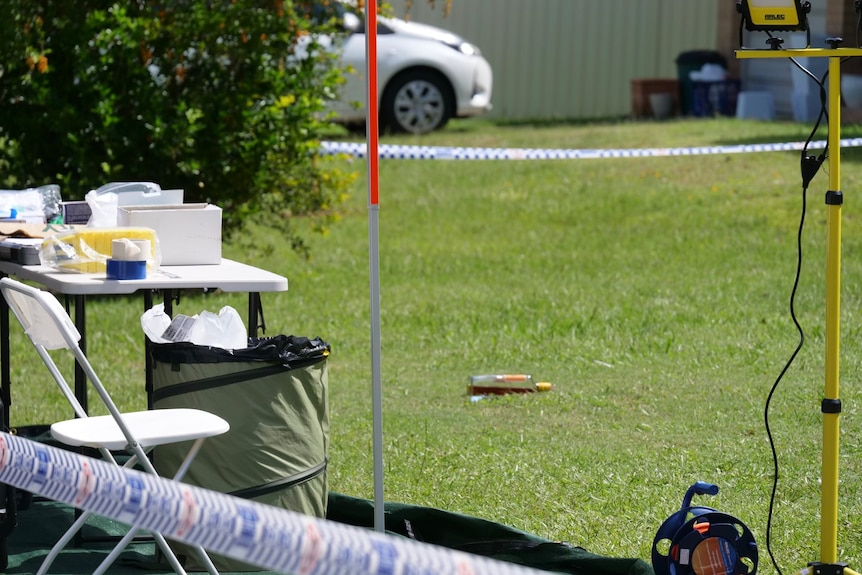 Crime scene tape, a table, lights and a rum bottle lying on the lawn.