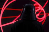 The back of Darth Vader as he looks a red glowing map.