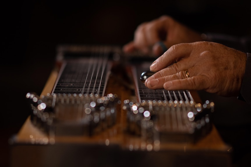 A photo of Lucky Ocean's hands playing the strings of pedal steel guitar.