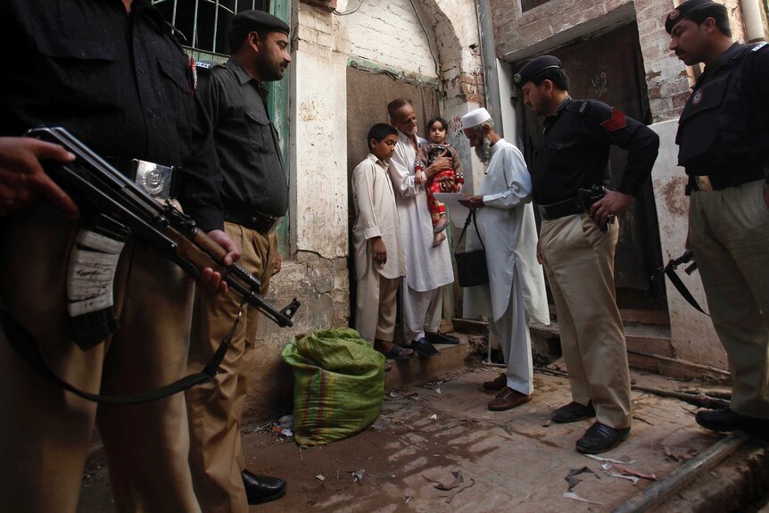 Police stand guard as a health worker visits homes during a polio vaccination campaign in Peshawar