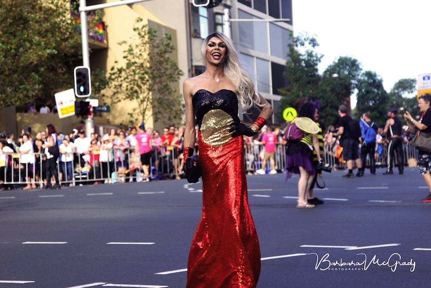 An attendee dressed in a sparkly Aboriginal flag desk smiles at the camera for Mardi Gras 2018.