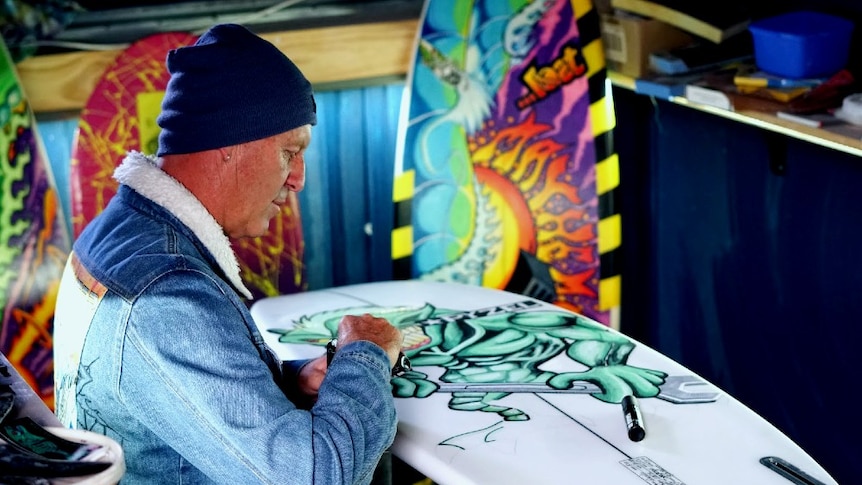 Jeremy Ievins looks down at a gremlin themed surfboard he's painting.