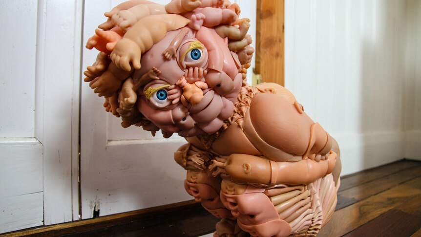 A squatting child sculpture made from doll parts