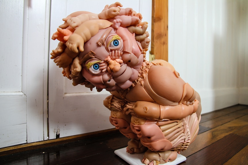 A squatting child sculpture made from doll parts