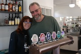 A woman and a man stand behind beer taps in a bar