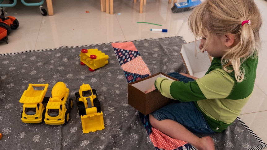 Meredith playing with a box and toy trucks.