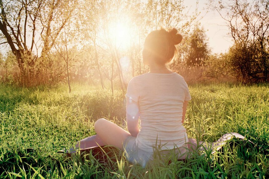 Woman sitting in the grass in a field with the sun low on the horizon