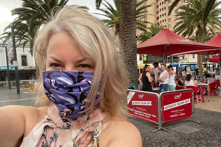 A woman wearing a face mask with a cafe and palm trees behind