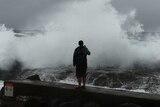 A man films large waves battering the coast at Snapper Rocks at Coolangatta