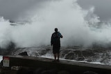 A man films large waves battering the coast at Snapper Rocks at Coolangatta