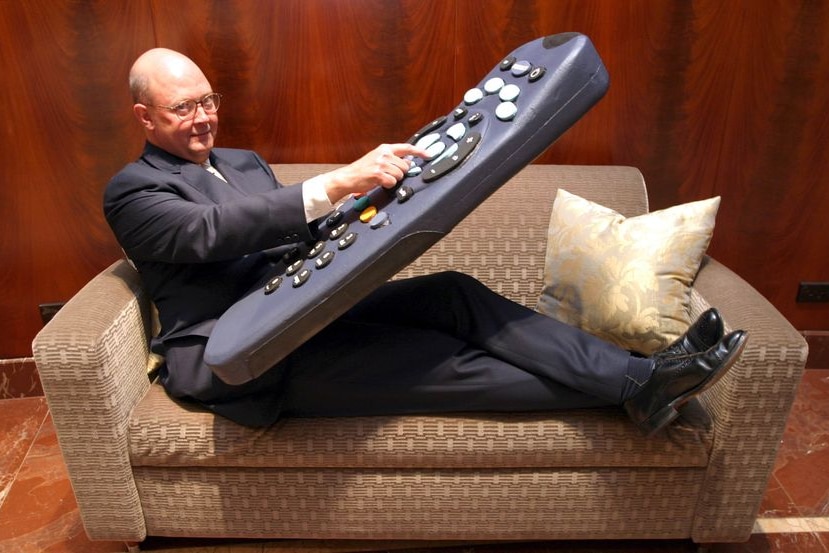 a man lies on a couch holding a giant human-sized remote
