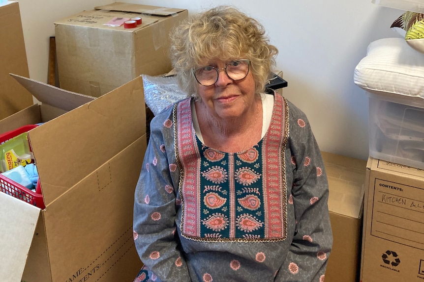 Ms Nichols sits in front of a pile of moving boxes.