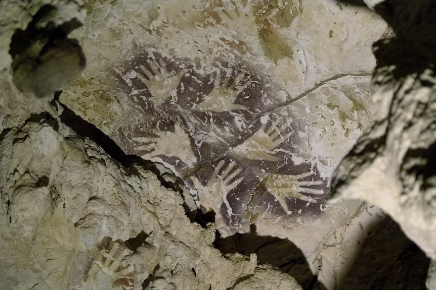 The outline of hands painted in dark red ochre on a cave wall