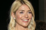 Holly Willoughby in a dress standing on a red carpet and smiling as fans stand behind a barrier behind her