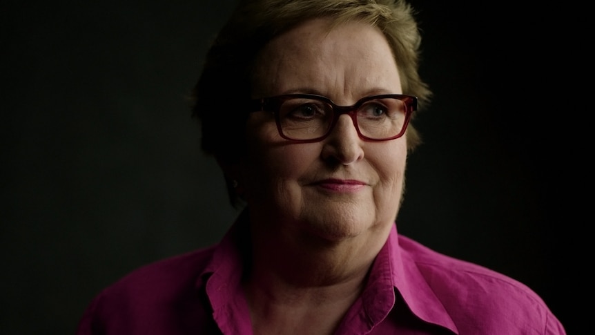 A portrait of a woman in hot pink and glasses, glancing to her left