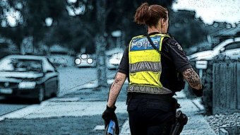 A female police officer walks along a suburban street carrying a can of pepper spray.