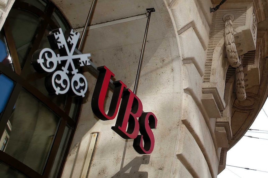 A Swiss national flag and a flag of the city of Basel fly over the entrance of a branch office of Swiss bank UBS