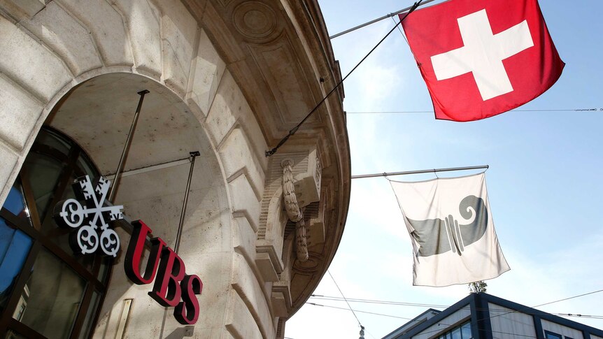 A Swiss national flag and a flag of the city of Basel fly over the entrance of a branch office of Swiss bank UBS