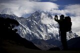 A tourist is silhouetted as he takes a pictures of Mount Nuptse (C) as Mount Everest is covered with clouds (L)