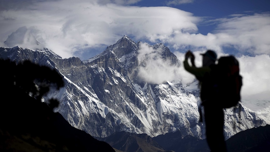 A tourist is silhouetted as he takes a pictures of Mount Nuptse (C) as Mount Everest is covered with clouds (L)