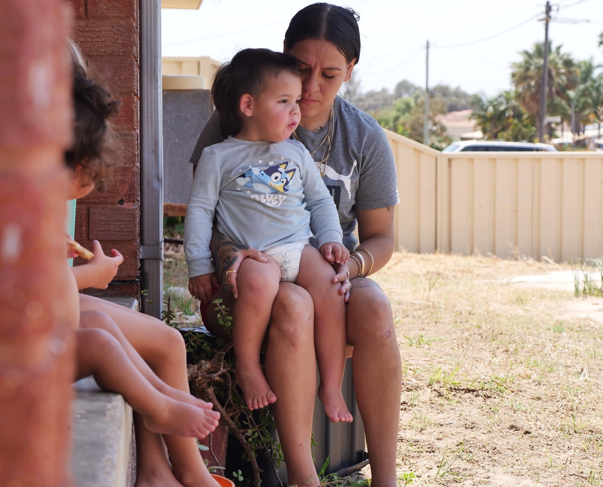 Mum with baby son sitting on lap. Legs of other children in foreground.