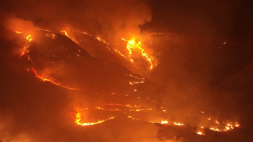 a night drone shots shows fire cutting through black hills