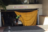 A policeman unfurls a tarpaulin over a car at the entrance to an underground carpark