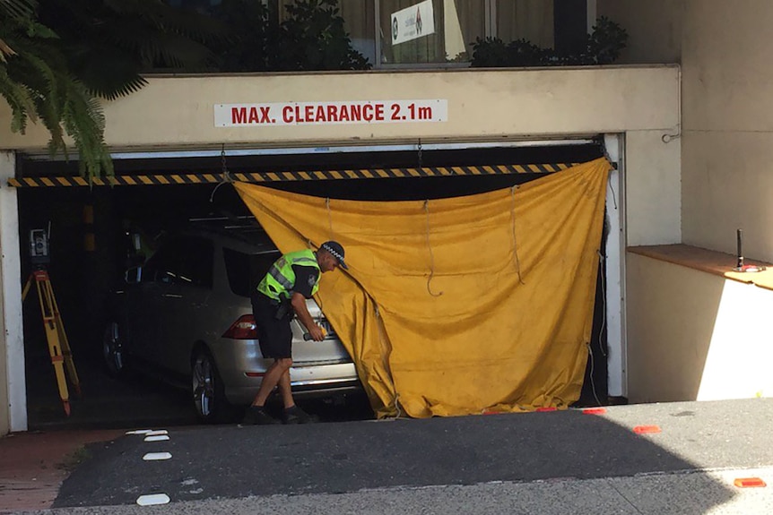 A policeman unfurls a tarpaulin over a car at the entrance to an underground carpark