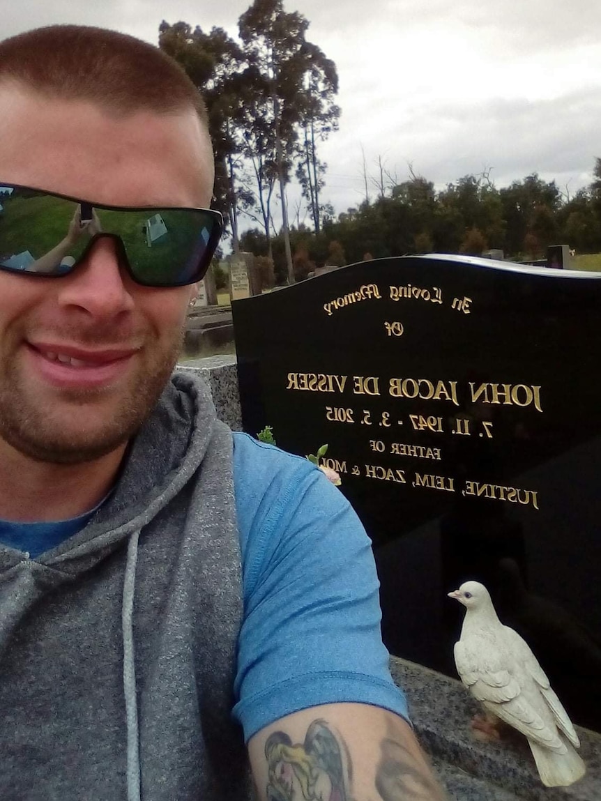 A man wearing sunglasses pictured with a grave headstone.