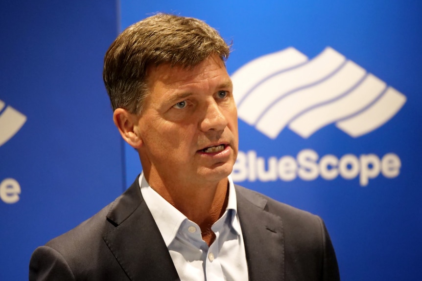 A man in a suit with short brown hair and a Bluescope logo in the background