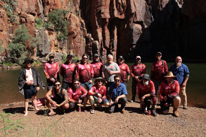 a group of men, some wearing pink shirts, stand in front of a gorge in WA's Pilbara