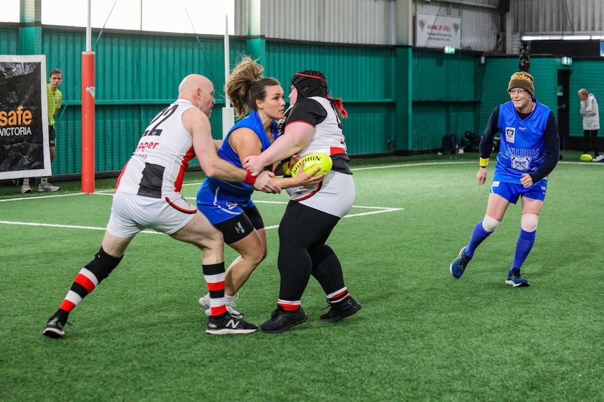 Two players tackle one player while on an indoor court playing AFL blind.