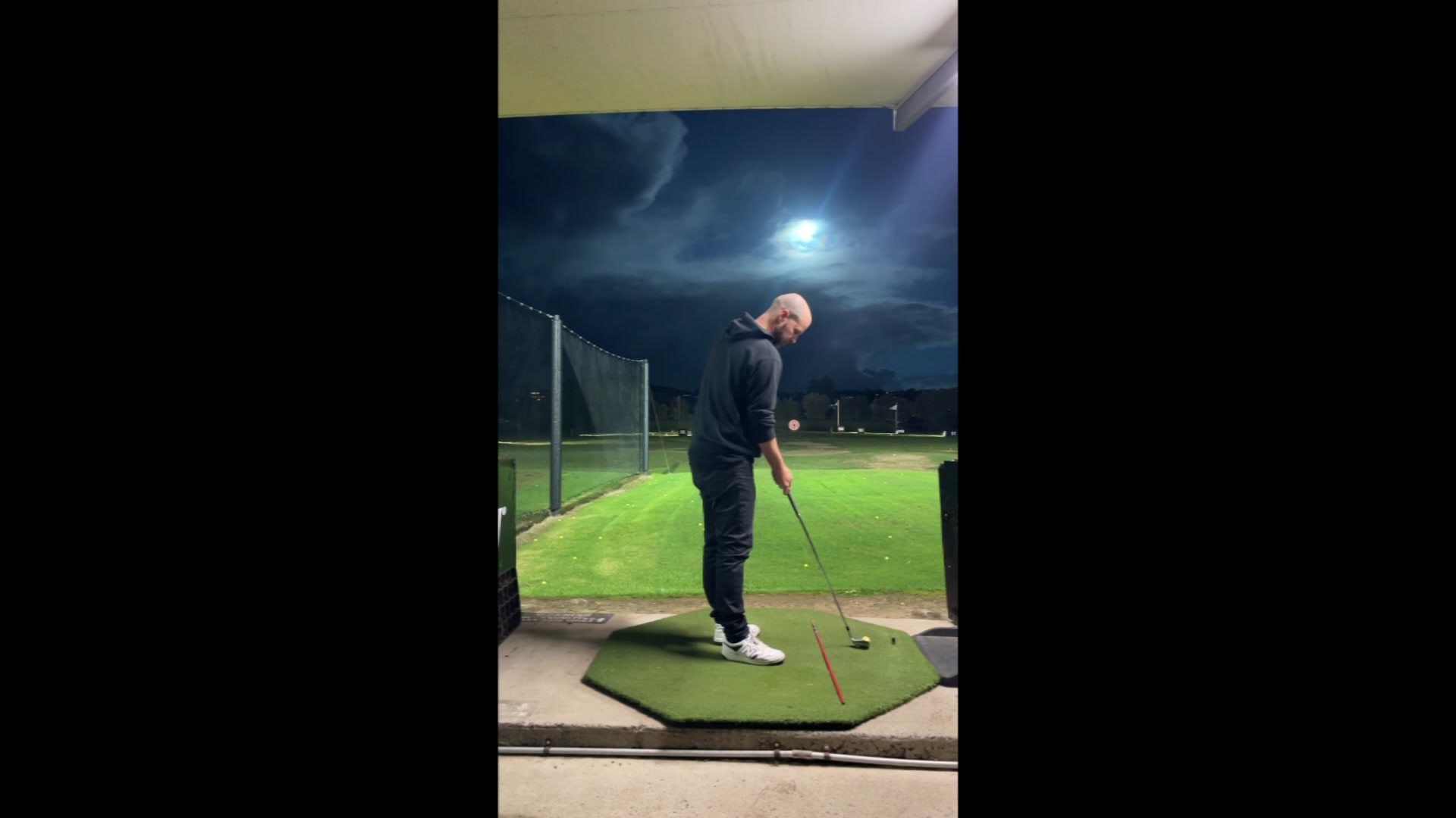 A golfer at a driving range lines up a shot as a meteor lights up the sky.