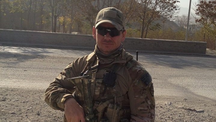 Commando Kevin Frost wearing army clothes and holding a gun on a gravel road in Afghanistan.