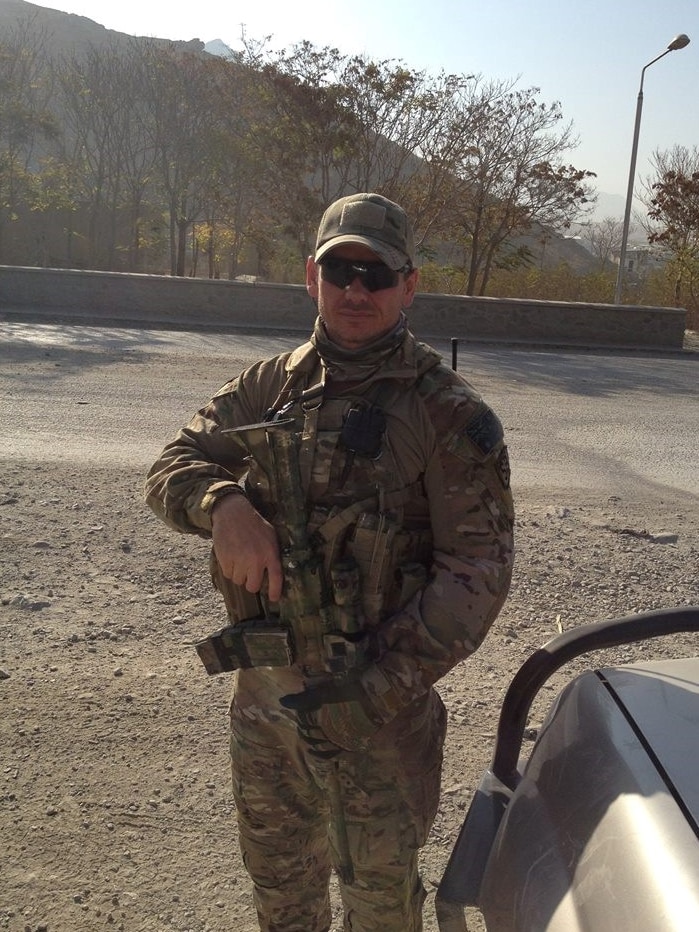 Commando Kevin Frost wearing army clothes and holding a gun on a gravel road in Afghanistan.