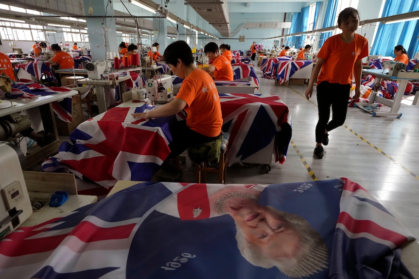 Muncitori în cămăși portocalii sunt văzuți plantând steaguri britanice într-o fabrică.