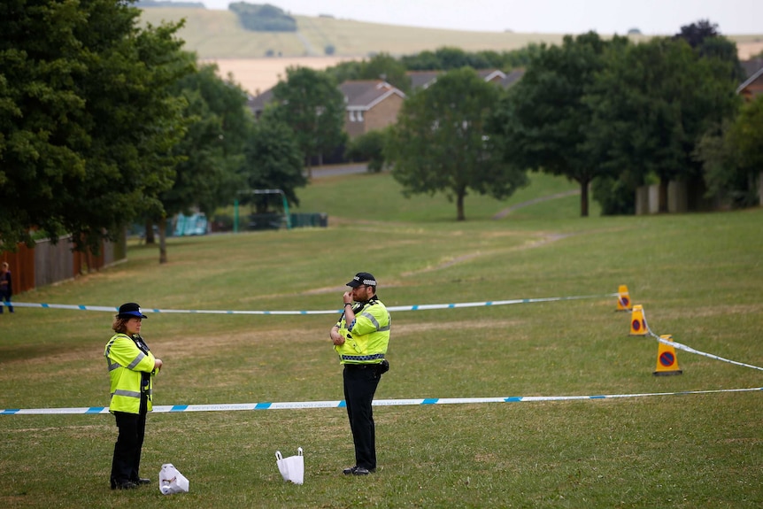 Police stand next to an area of a field that is cordoned off.