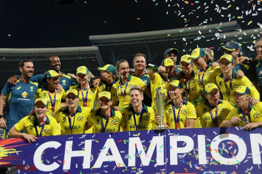 Australia's cricketers celebrate behind a 'CHAMPIONS' banner and lift a trophy as confetti flies.