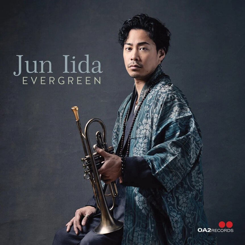 A colour photo of trumpeter Jun Iida in a Japanese-style garb; he's holding his trumpet