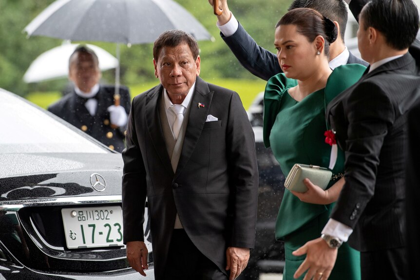 Rodrigo Duterte in a suit walks next to his daughter Sara in an emerald evening gown 
