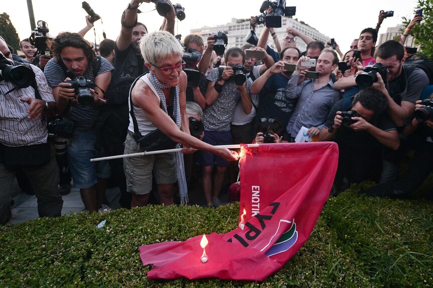 A woman burns the flag of the ruling party Syriza, surrounded by journalists, in front of the Greek parliament in Athens