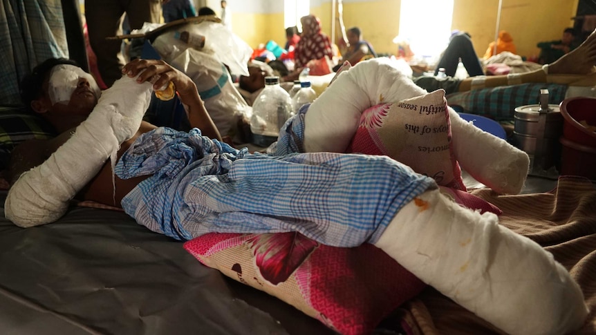 A man with both eyes, one hand and both legs bandaged lies on a hospital floor.