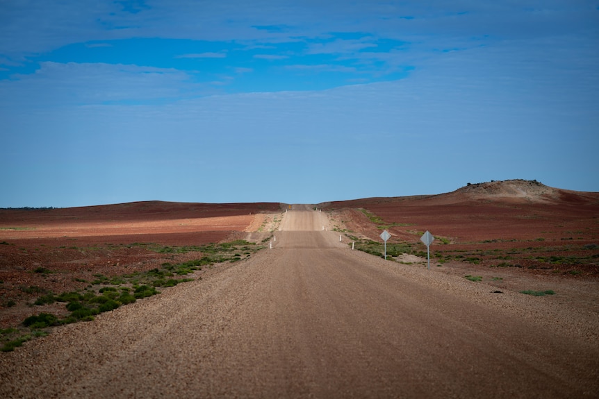 A main road cuts through the South Australian outback and desert, with clear blue sky above