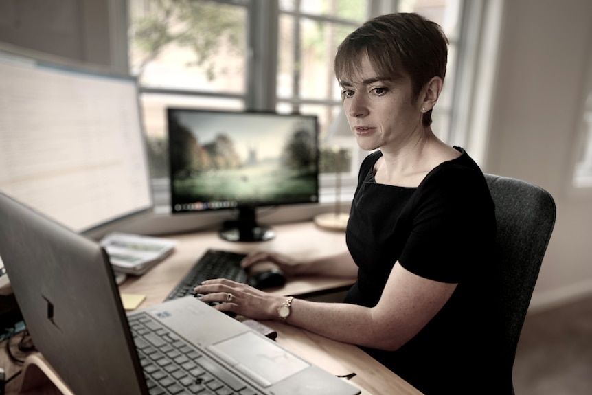 Sarah con un vestido negro, sentada escribiendo en su computadora en su casa en Sydney en noviembre de 2021.