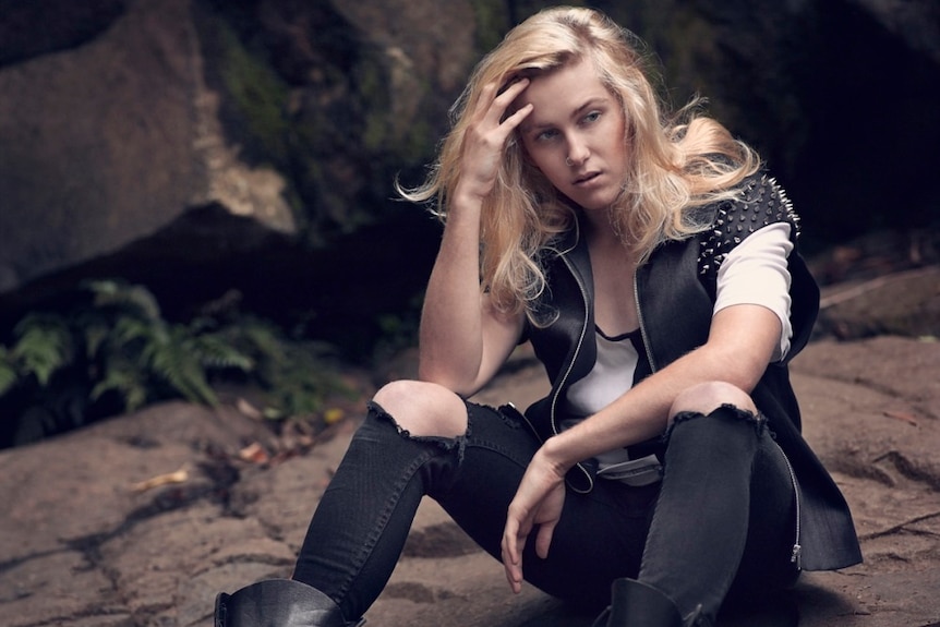 An androgynous model wears ripped black jeans, white t-shirt, and black studded vest