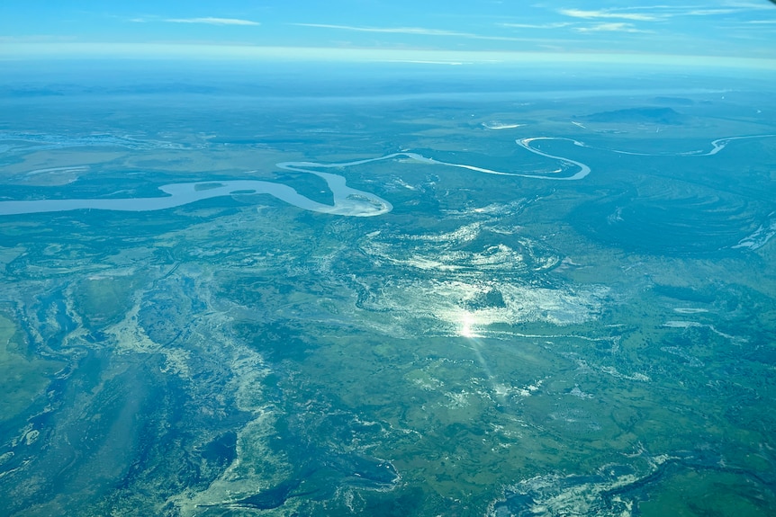 A wide aerial landscape image featuring green vegetation and a snaking blue river