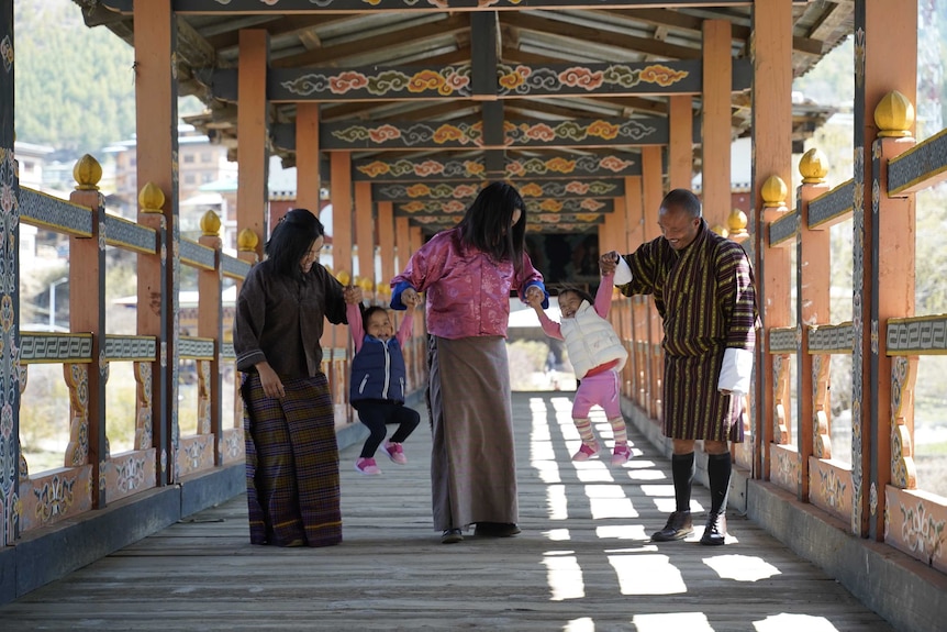 Two toddlers giggle as they are lifted up by three adults in a wooden walkway