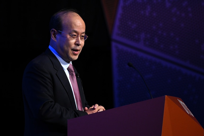 Xiao Qian speaks from a podium at an event. 