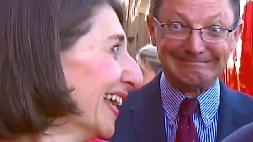 Three politicians at a press conference, one pulling an awkward face