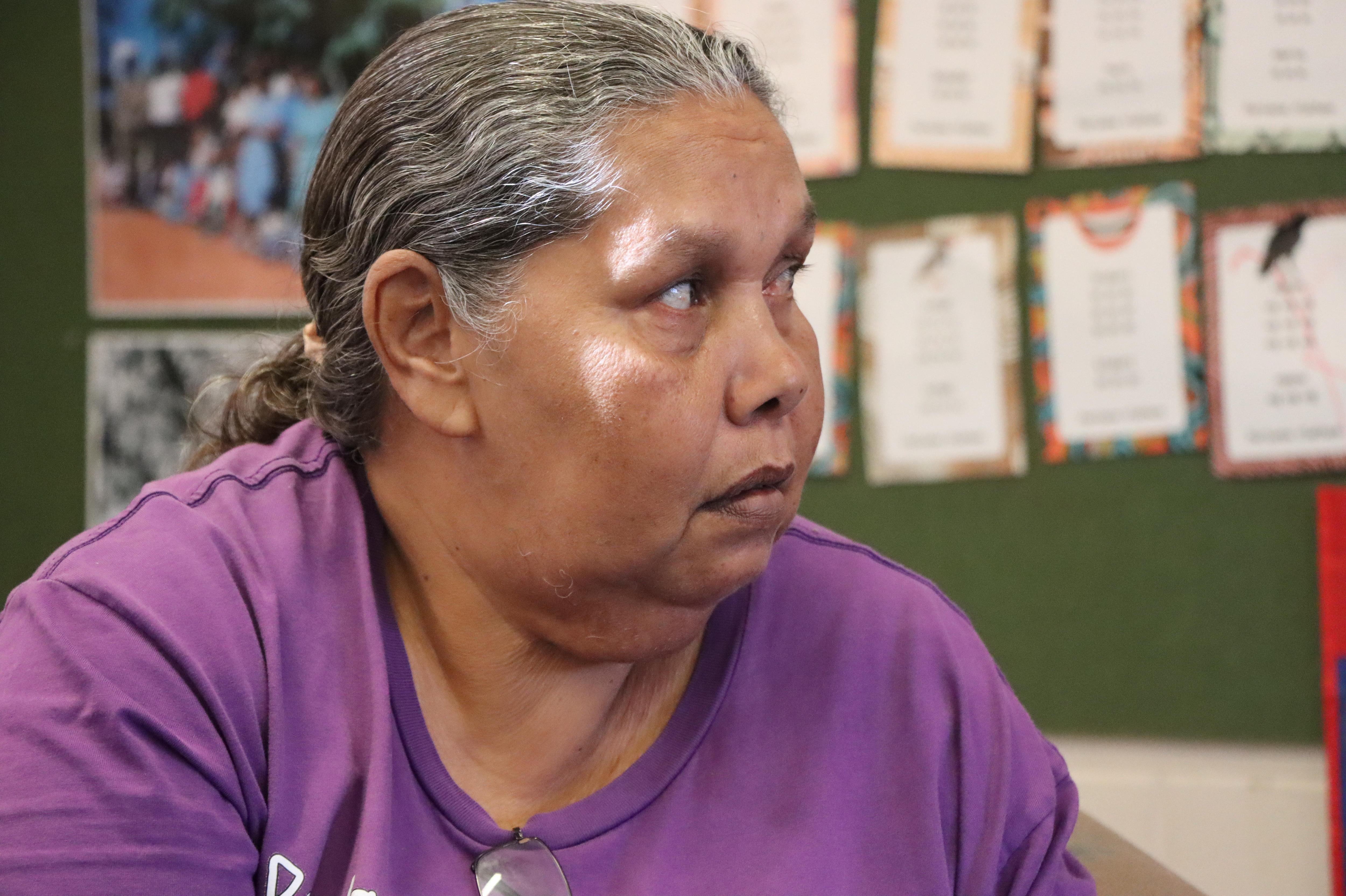A woman in a purple t shirt looks to her left.